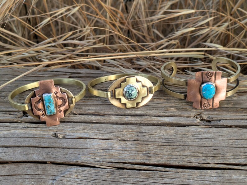 May include: Three brass bracelets with turquoise stones set in copper. Each bracelet features a different design, including a cross, a square, and a diamond pattern.