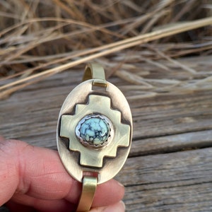 May include: A brass bracelet with a turquoise stone set in a cross design.