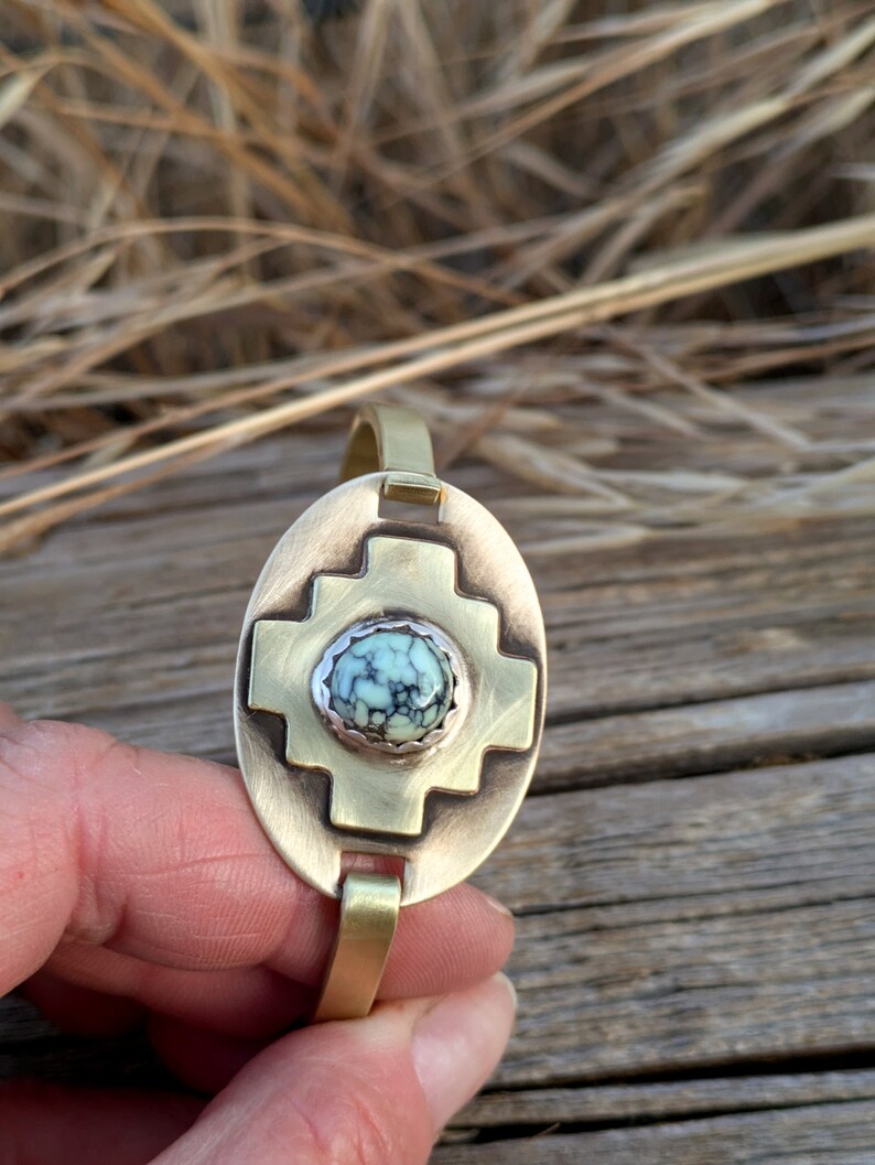 May include: A brass bracelet with a turquoise stone set in a cross design.