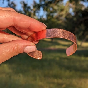 K&ouml;nnte beinhalten: Ein geh&auml;mmertes Kupferarmband mit glatter, abgerundeter Oberfl&auml;che. Das Armband hat eine warme, rotbraune Farbe.