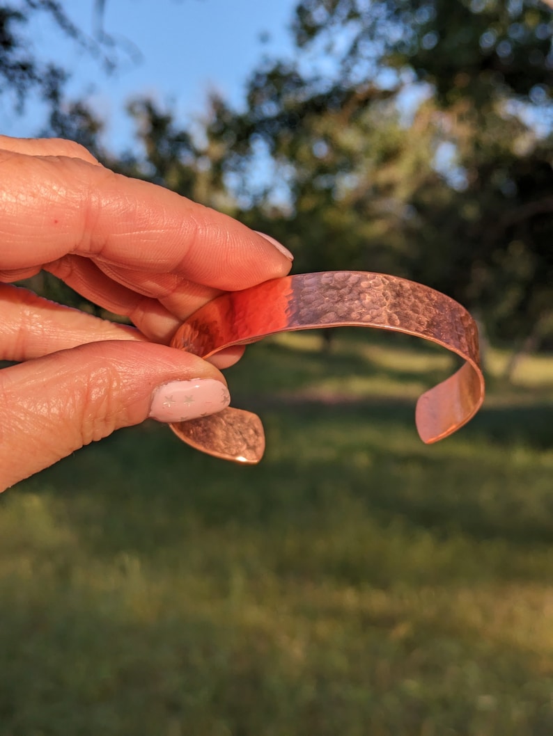 K&ouml;nnte beinhalten: Ein geh&auml;mmertes Kupferarmband mit glatter, abgerundeter Oberfl&auml;che. Das Armband hat eine warme, rotbraune Farbe.