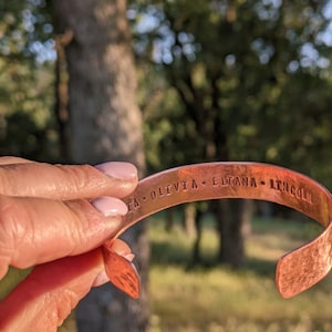 K&ouml;nnte beinhalten: Ein Kupferarmband mit der Gravur "ITA OLIVIA ELTANA LINCOLN" auf der Au&szlig;enseite.