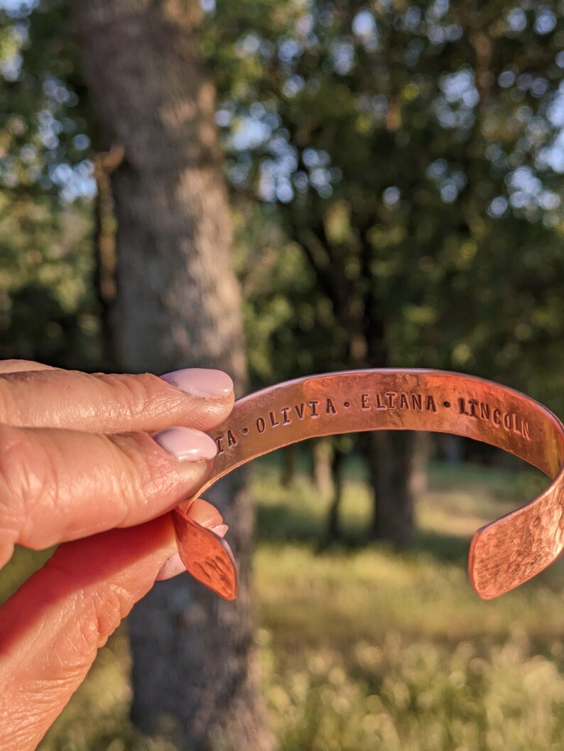 K&ouml;nnte beinhalten: Ein Kupferarmband mit der Gravur "ITA OLIVIA ELTANA LINCOLN" auf der Au&szlig;enseite.