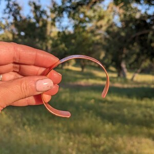 K&ouml;nnte beinhalten: Ein Kupferarmband mit glatter, polierter Oberfl&auml;che. Das Armband ist offen und hat eine leicht gebogene Form.