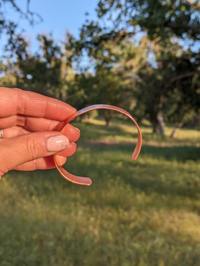 K&ouml;nnte beinhalten: Ein Kupferarmband mit glatter, polierter Oberfl&auml;che. Das Armband ist offen und hat eine leicht gebogene Form.