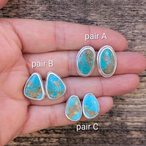 May include: Three pairs of turquoise stud earrings with silver settings. Pair A has oval stones, pair B has triangular stones, and pair C has teardrop-shaped stones. The turquoise stones have a mix of blue and brown hues.