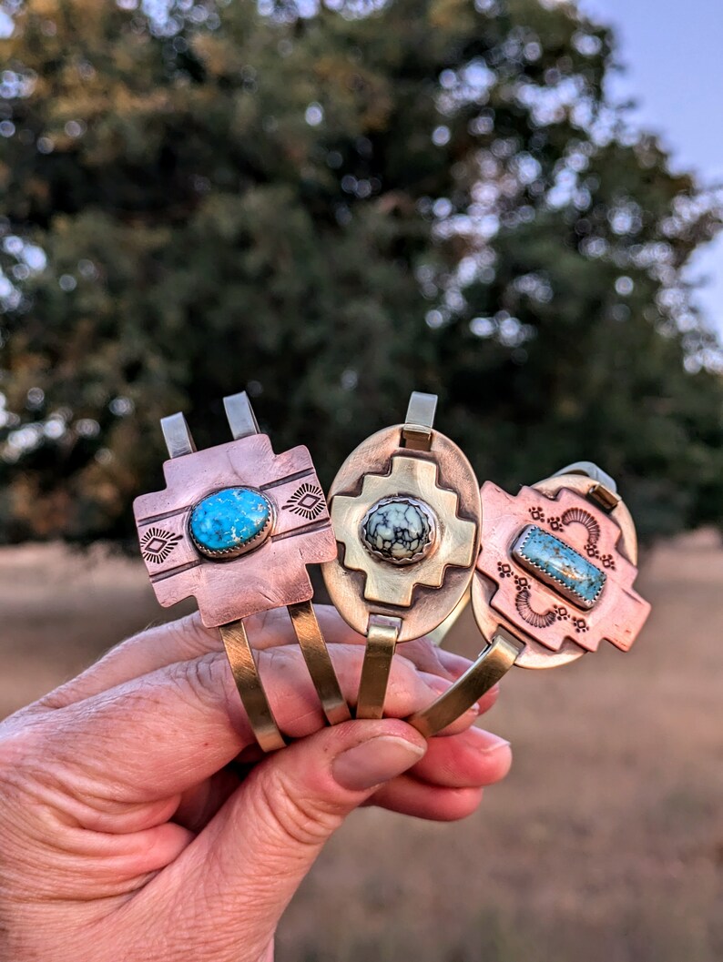 May include: Three brass and copper bracelets with turquoise stones. Each bracelet features a different design with a turquoise stone in the center.