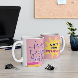 May include: Two white ceramic mugs with pink backgrounds. One mug features the blue text "I'm an Executive Assistant" with a small white flower. The other mug displays a yellow starburst graphic with the blue text "WHAT'S YOUR SUPERPOWER?"