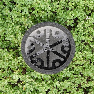 May include: A black and white circular patch with a geometric design on a green background.
