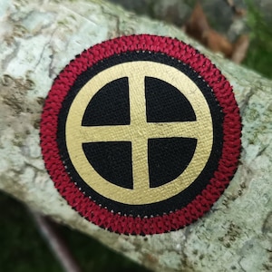 May include: A red and gold embroidered patch with a black background and a gold cross inside a circle.