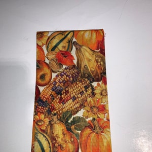 May include: A fabric with a fall harvest theme. The fabric features gourds, pumpkins, corn, and flowers in shades of orange, yellow, brown, and green.