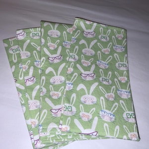 May include: Set of six green fabric napkins with a white bunny rabbit wearing glasses pattern.