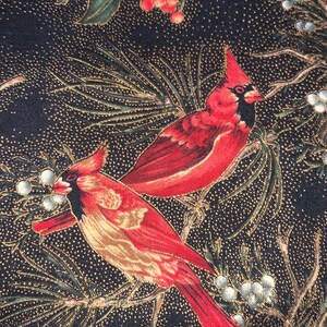 May include: A fabric featuring two red cardinal birds perched among pine needles, berries, and white accents. The background is a dark navy blue with gold speckles, creating a festive and nature-inspired design.