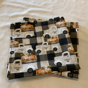May include: Set of three black and white checkered fabric napkins with a white truck carrying pumpkins and the word "HARVEST" printed on each napkin.