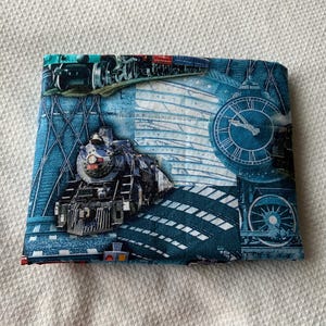 May include: A blue and white fabric with a train and clock design. The train is a steam engine with a black and red color scheme. The clock is a large, round clock with Roman numerals.