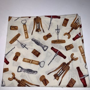 May include: A white fabric kitchen towel with a repeating pattern of corkscrews, bottle openers, and wine corks. The pattern is in shades of brown, red, and gray.