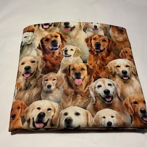 May include: A fabric item featuring a collage of Golden Retriever dogs in various poses. The dogs have brown and cream-colored fur, with some showing their tongues. The item is likely a pillow or fabric panel.