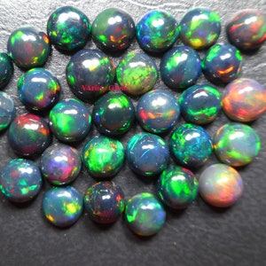 May include: A collection of 30 round black opal cabochons, each displaying a variety of iridescent colours, including green, red, and blue.
