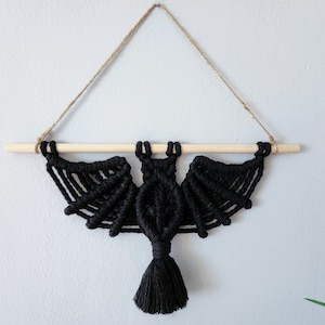May include: Black macrame bat wall hanging with a wooden dowel and a tassel.