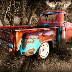 May include: A rusty blue and red vintage pickup truck parked in a field. The truck is partially obscured by trees and tall grass.