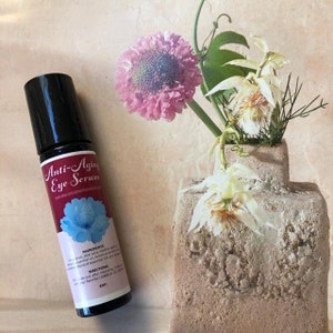May include: A black roller bottle with a red label that says "Anti-Aging Eye Serum". The label also includes a blue flower graphic and the ingredients and directions for use.