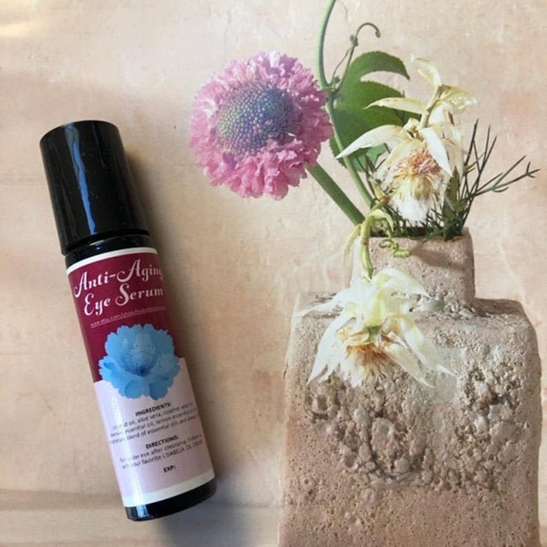 May include: A black roller bottle with a red label that says "Anti-Aging Eye Serum". The label also includes a blue flower graphic and the ingredients and directions for use.