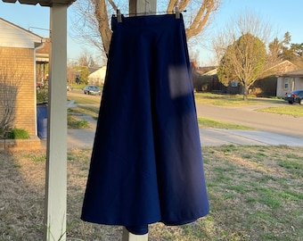 May include: A dark blue skirt hanging on a hanger on a porch. The skirt is a-line and has a high waist.