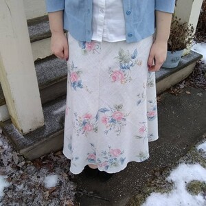 May include: A white skirt with a floral pattern, worn with a light blue cardigan and a white button-down shirt.
