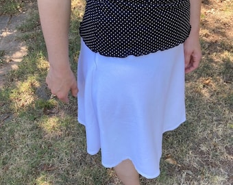 May include: A white skirt with a flowy, A-line silhouette. The skirt is made of a lightweight fabric and has a simple, casual design.