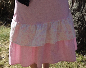 May include: A pink and white tiered skirt with a ruffled hem. The skirt is made of a lightweight fabric and has a floral print.