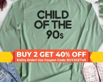 May include: A sage green long-sleeve shirt featuring the black text "CHILD OF THE 90s" printed in a bold, rounded sans-serif font across the center of the chest. The garment has a crew neckline and long sleeves with ribbed cuffs.