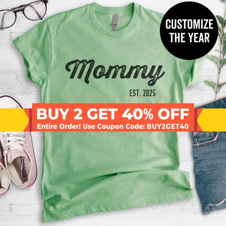 May include: Green t-shirt with the text "Mommy Est. 2025" in black. The text is in a cursive font. There is a yellow banner at the bottom of the image that says "BUY 2 GET 40% OFF Entire Order! Use Coupon Code: BUY2GET40"