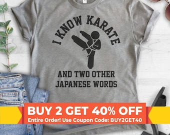 May include: A heather gray short-sleeve t-shirt featuring a black graphic of a person performing a karate kick. The text reads I KNOW KARATE AND TWO OTHER JAPANESE WORDS in a bold, black, sans-serif font centered on the chest of the garment.