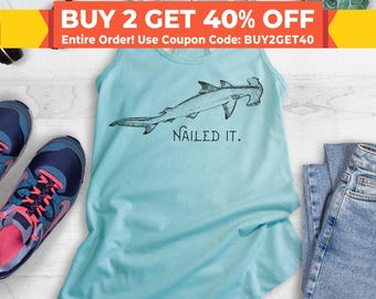 May include: A light blue tank top with a hammerhead shark illustration and the text "Nailed It." The tank top is paired with blue jeans and athletic shoes. The image also includes a banner that says "BUY 2 GET 40% OFF".