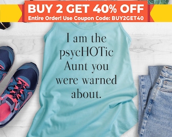 Puede incluir: Un top de tirantes azul claro con el texto "I am the psycHOTic Aunt you were warned about." El top está sobre una superficie de madera blanca con un par de pantalones vaqueros azules, un par de zapatillas de deporte rosa y azules y una planta suculenta.