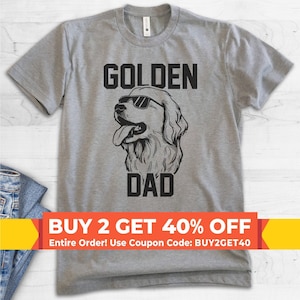 May include: A heather gray short-sleeved t-shirt featuring a black graphic of a golden retriever wearing sunglasses. The text GOLDEN is printed above the dog illustration and the text DAD is printed below it in a bold, black sans-serif font.