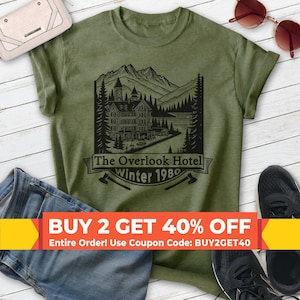 May include: A green t-shirt with a black graphic of a mountain scene with a building and the text "The Overlook Hotel winter 1980".