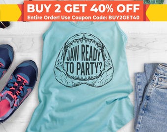 May include: A light blue tank top with a black graphic of a shark's open mouth with the text "JAW READY TO PARTY?" printed on it. The tank top is on a white surface with a pair of blue jeans and a pair of running shoes.