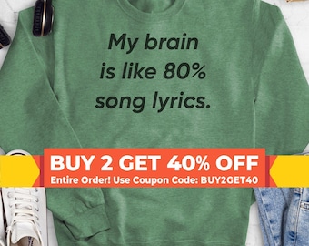 May include: A heather green crewneck sweatshirt featuring the black text "My brain is like 80% song lyrics." The long-sleeved garment has a ribbed collar, cuffs, and hem, with a solid, textured fabric finish across the front and sleeves.