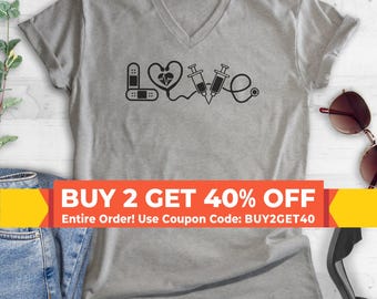 May include: A heather gray V-neck t-shirt featuring a black graphic design that spells the word LOVE. The letter L is formed by a bandage, the O is a heart with an EKG line, the V is two syringes, and the E is a stethoscope end piece.