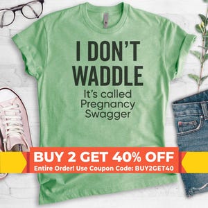 May include: A light green short-sleeved t-shirt featuring the black text I DON'T WADDLE It's called Pregnancy Swagger. The shirt is displayed with a pair of white sneakers and blue denim jeans, with a promotional banner across the bottom.