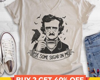 May include: A beige V-neck t-shirt featuring a black graphic illustration of Edgar Allan Poe holding a teacup with a raven perched on his shoulder. Below the illustration, a banner displays the text: POE SOME SUGAR ON ME.