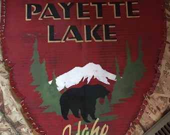 May include: A red wooden sign with a white mountain, green trees, and a black bear silhouette. The sign reads "EST. 1930 PAYETTE LAKE Idaho".