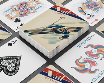 May include: A deck of playing cards featuring a vintage Vail, Colorado ski resort design. The deck shows a skier in action, with the word "Vail" in red and blue. Other cards include a King of Clubs, Ace of Spades, and a Joker card.