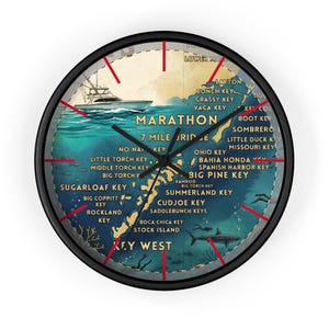 May include: Round wall clock with a black frame. The clock face features a map of the Florida Keys with a boat, fish, and the names of the keys. The clock hands are black, and the hour markers are red.