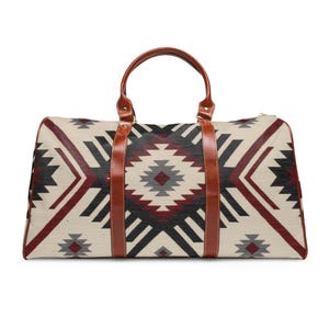 Puede incluir: Una bolsa de viaje rectangular con un patrón geométrico en crema, negro, gris y burdeos. Tiene asas y correas de cuero marrón y una cremallera dorada. La bolsa está diseñada para viajar y tiene un aspecto clásico y elegante.