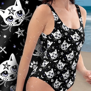 Op de afbeelding: Zwarte badpak met een witte kattenprint. De kat heeft een pentagram op zijn voorhoofd en grote, blauwe ogen. De achtergrond is zwart met witte sterren, manen en kruisen.