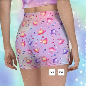 May include: Pink and purple shorts with a galaxy print featuring spaceships and stars. The shorts have an elastic waistband and are available in sizes XS to 3XL.