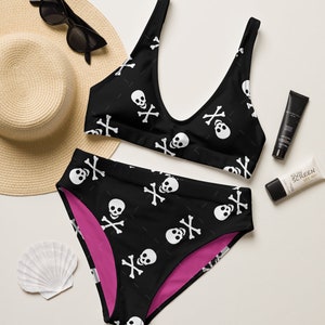 May include: Black and white skull and crossbones print bikini top and high-waisted bottoms. The bikini top has a scoop neck and the bottoms have a pink lining.