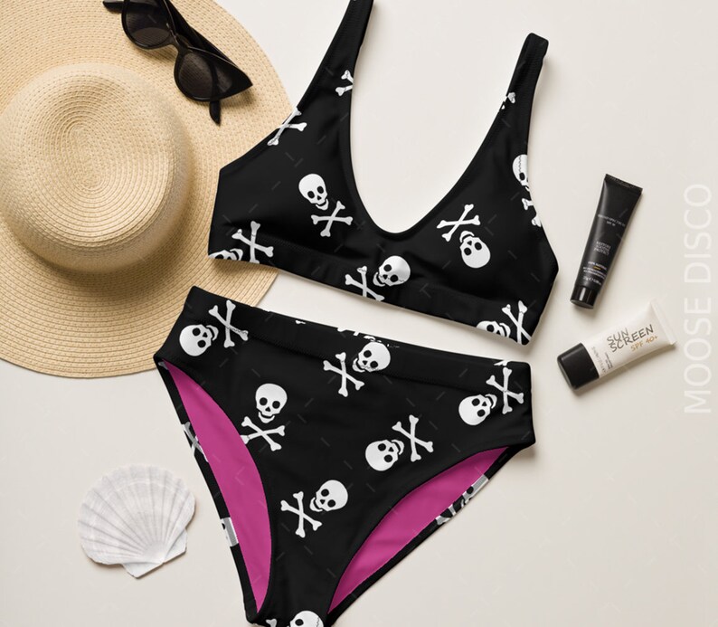 May include: Black and white skull and crossbones print bikini top and high-waisted bottoms. The bikini top has a scoop neck and the bottoms have a pink lining.